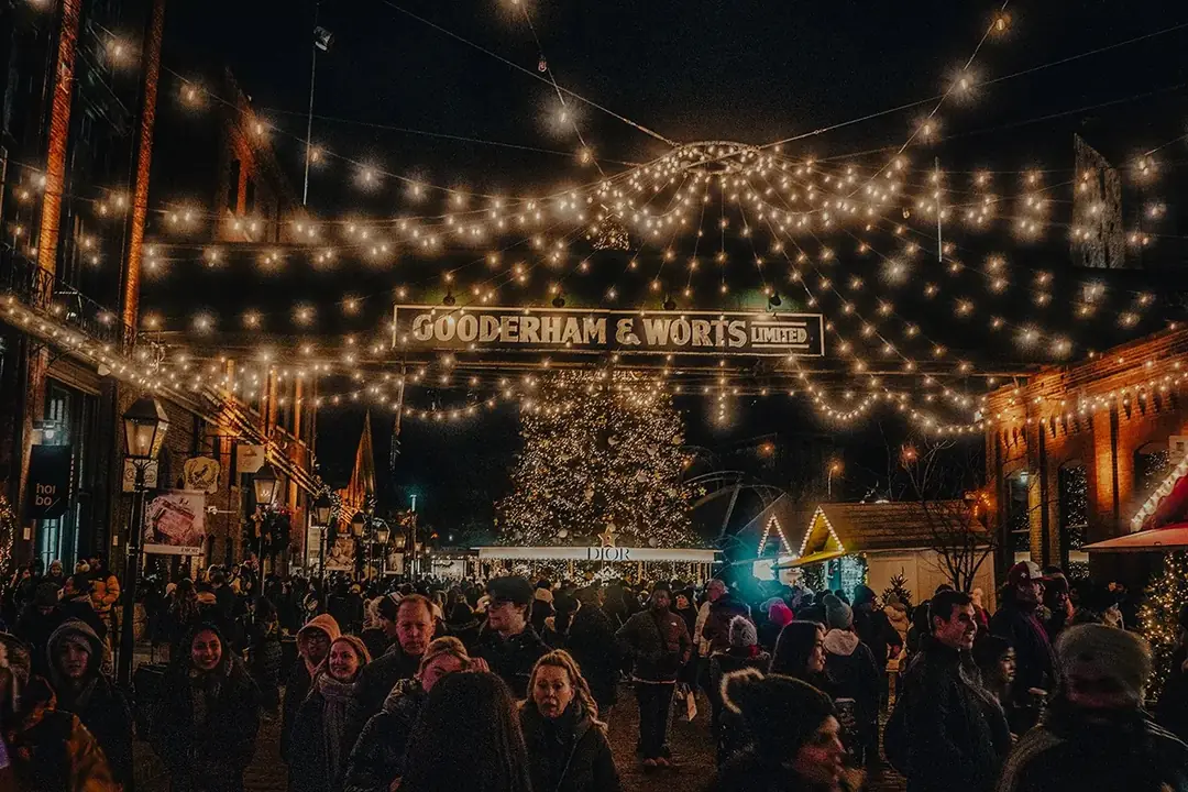 String lights over crowds beneath the Gooderham & Worts sign at the Distillery Winter Village