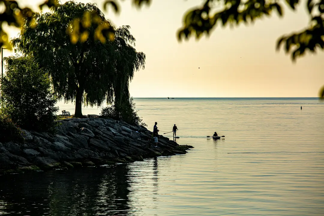 Golden-hour light over the Port Credit shoreline, with a paddleboarder and kayaker on the lake